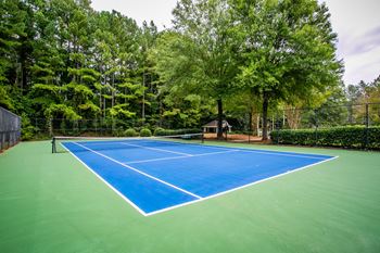 a tennis court with blue and green turf and trees